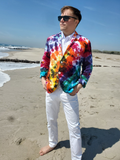 Man wearing a colorful tie-dye blazer and white pants on a beach.