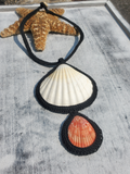 A handmade bold statement necklace featuring two seashell pendants. A very large white one and an orange one, worked on black cordweathered white wooden surface.ent 