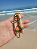 Hand holding a beaded necklace with a beach and ocean in the background