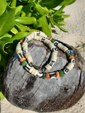 Beaded necklace with decorative elements on a stone surface with greenery in the background