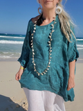 Woman in teal top and white pants standing on a beach with ocean waves in the background