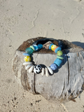 Beaded bracelet with colorful beads on a piece of driftwood on a sandy surface