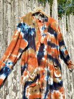 Tie-dye cardigan with orange, blue, and brown patterns hanging against a wooden fence.