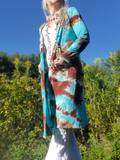 Person wearing a tie-dye cardigan in a natural setting with greenery and blue sky.