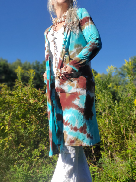 Person wearing a tie-dye cardigan in a natural setting with greenery and blue sky.