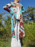 Person wearing a tie-dye cardigan in a natural setting with trees and blue sky.