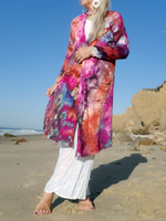 Person wearing an Ice dye cardigan on a beach with ocean and rocks in the background