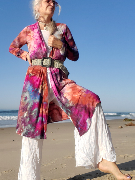 A person wearing a colorful cardigan and white pants on a beach