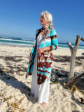 Woman standing on a sandy beach wearing a colorful tie-dye cardigan.