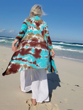 Woman walking on a beach wearing a colorful tie-dye cover-up over a white dress.