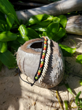 Coconut shell with a beaded necklace on a sandy surface with greenery