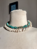 Necklace with turquoise stones and shells on a mannequin bust against a neutral background.