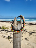 Colorful beaded shell necklace on a wooden post with a beach and ocean background