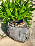 Choker with colorful beads on a wooden container against green leaves