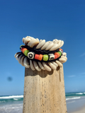 Colorful beaded bracelet on a wooden post with a beach and blue sky in the background