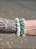 Person wearing multiple bracelets on a tattooed wrist with a blurred background