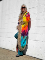 Person wearing a colorful tie-dye outfit with fur trim against a white wall.
