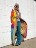 Person wearing a colorful tie-dye cardigan with fur trim against a white wall.