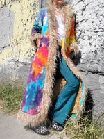 Person wearing a colorful tie-dye coat with fur trim against a rocky background