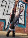 Person wearing a colorful jacket and black boots in front of a graffiti-covered wall.