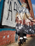 Person wearing a tie-dye coat standing in front of a graffiti-covered wall.
