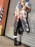 Person wearing a tie-dye coat standing against a metal shutter.