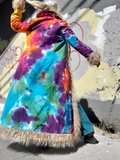 Person wearing a colorful tie-dye coat with fur trim against a graffiti-covered wall.