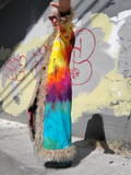 Person wearing a colorful tie-dye outfit with a fur-lined hood against a graffiti-covered wall.