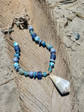 Necklace with blue beads and a shell on a sandy background