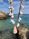 shell necklace with an orange shell pendant held up at the sea