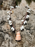 white shell clusters worked on a hemp rope, with an orange shell pendant on the rocks