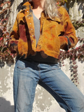 Person wearing a tie dye jacket and blue jeans standing against a textured wall.