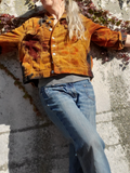 Person wearing a mustard yellow corduroy jacket and blue jeans leaning against a stone wall.