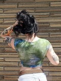 Person wearing a green and blue patterned top against a brick wall. a back shot of this crop top