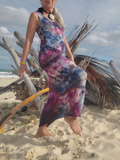 Woman in a tie-dye dress standing on a sandy beach with palm leaves in the background