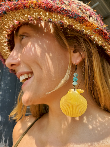 Woman wearing a colorful straw hat and yellow shell earrings outdoors.