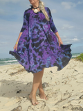Person wearing a purple and black patterned dress on a beach