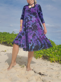 Woman wearing a purple and black patterned dress on a beach.