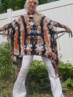 Person wearing a tie-dye poncho with fringe, standing outdoors.
