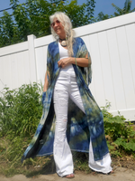 Woman wearing a long, colorful shawl over a white outfit in an outdoor setting.