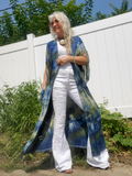 Woman wearing a long, colorful shawl over a white outfit in an outdoor setting.