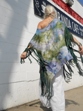 Person wearing a colorful fringe poncho in front of a cafe sign. A back shot.