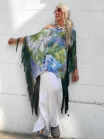 Person wearing a colorful poncho with fringe against a white wall