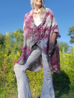 Person wearing a tie-dye shawl in a natural setting with greenery and blue sky.