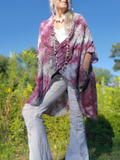 Person wearing a tie-dye shawl in a natural setting with greenery and blue sky.