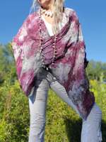 Person wearing a purple and white tie-dye shawl in a natural setting with greenery and blue sky.