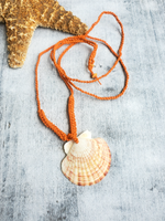 Orange waxed cotton cord crocheted necklace with a scallop shell pendant  on a textured surface
