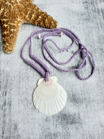 Adjustable lilec cord crocheted necklace with a white shell pendant on a textured surface