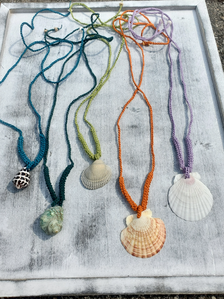 Five necklaces with shell pendants on a textured surface