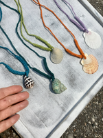 Colorful necklaces with shell pendants on a textured surface. my hand is on the picture to illustrate the size of the shell pendants.